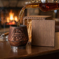 Whiskey being poured into a personalized charred oak tumbler beside an engraved wooden presentation box.
