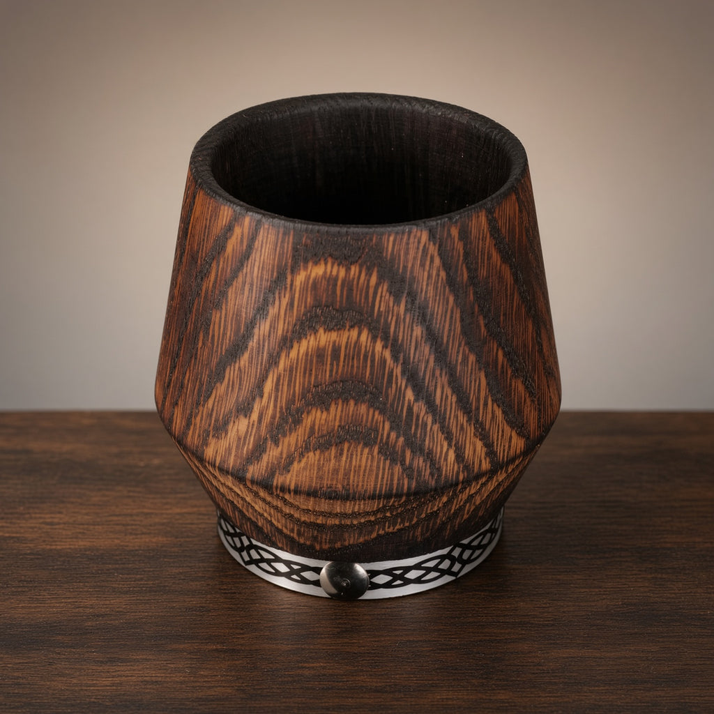 Charred oak whiskey glass with metal band on a dark wooden surface.