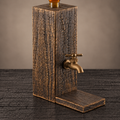 Charred oak whiskey dispenser with gold patina, a brass tap and a wooden platform on a black wood surface.