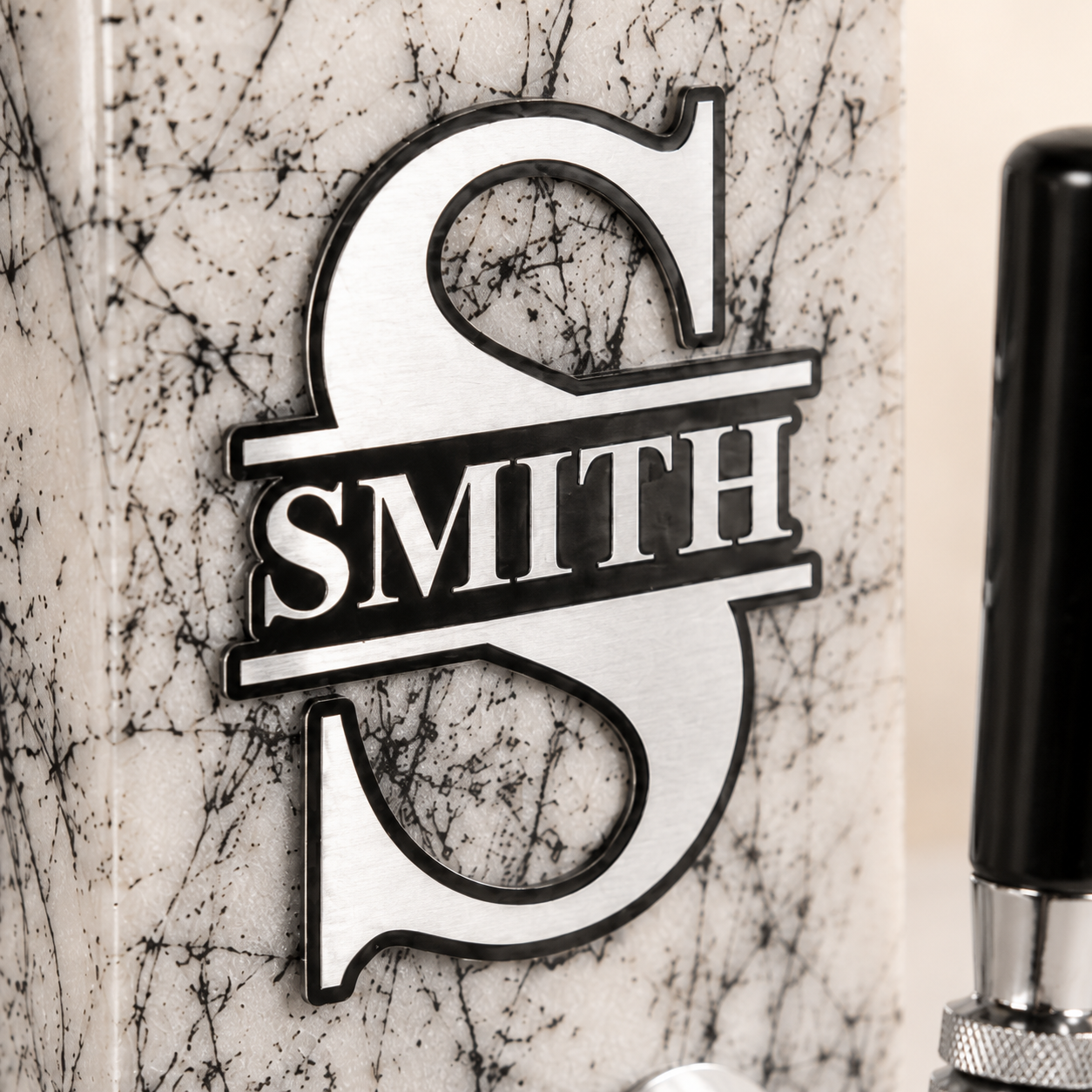 Close-up of engraved aluminum plaque on a personalized white marble whiskey dispenser, showing a custom family name design.