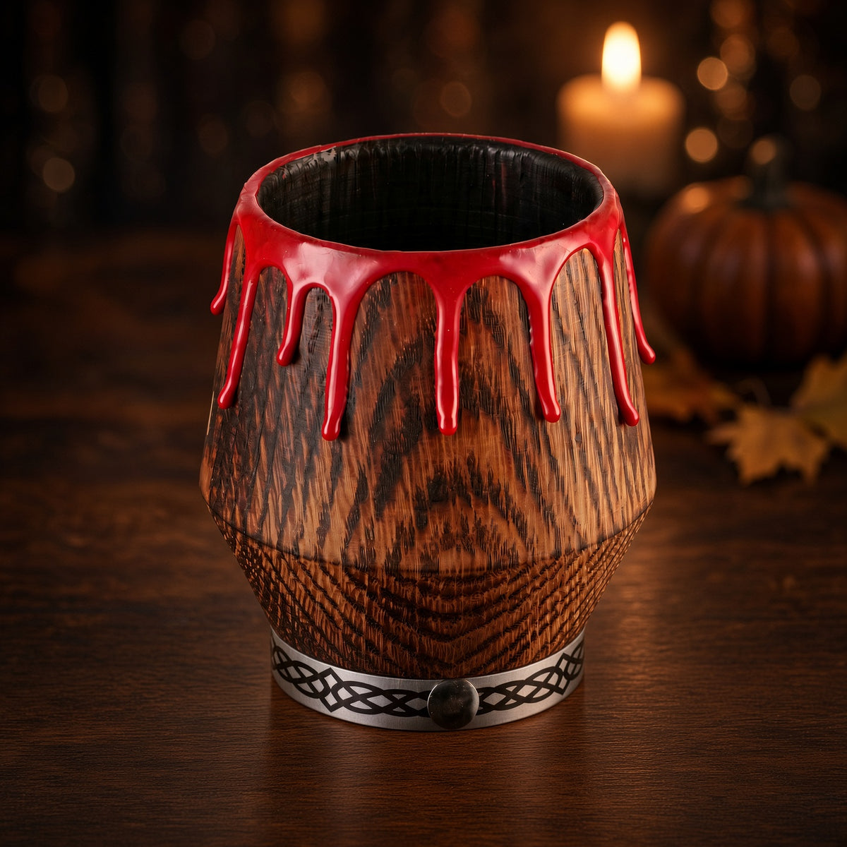 Red drip oak whiskey glass on a dark wooden table with a softly blurred candle and autumn leaves behind it.