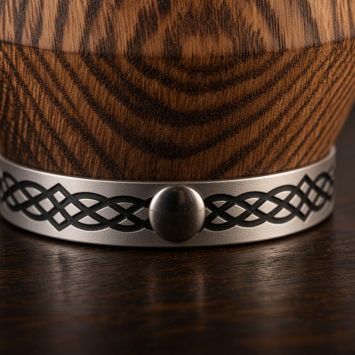 Close-up of the silver metal base with a black knot pattern and round rivet beneath the textured oak body.