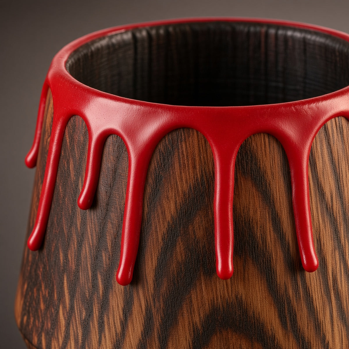 Close-up of the glossy red drip rim, dark interior, and oak grain of a wooden whiskey glass.