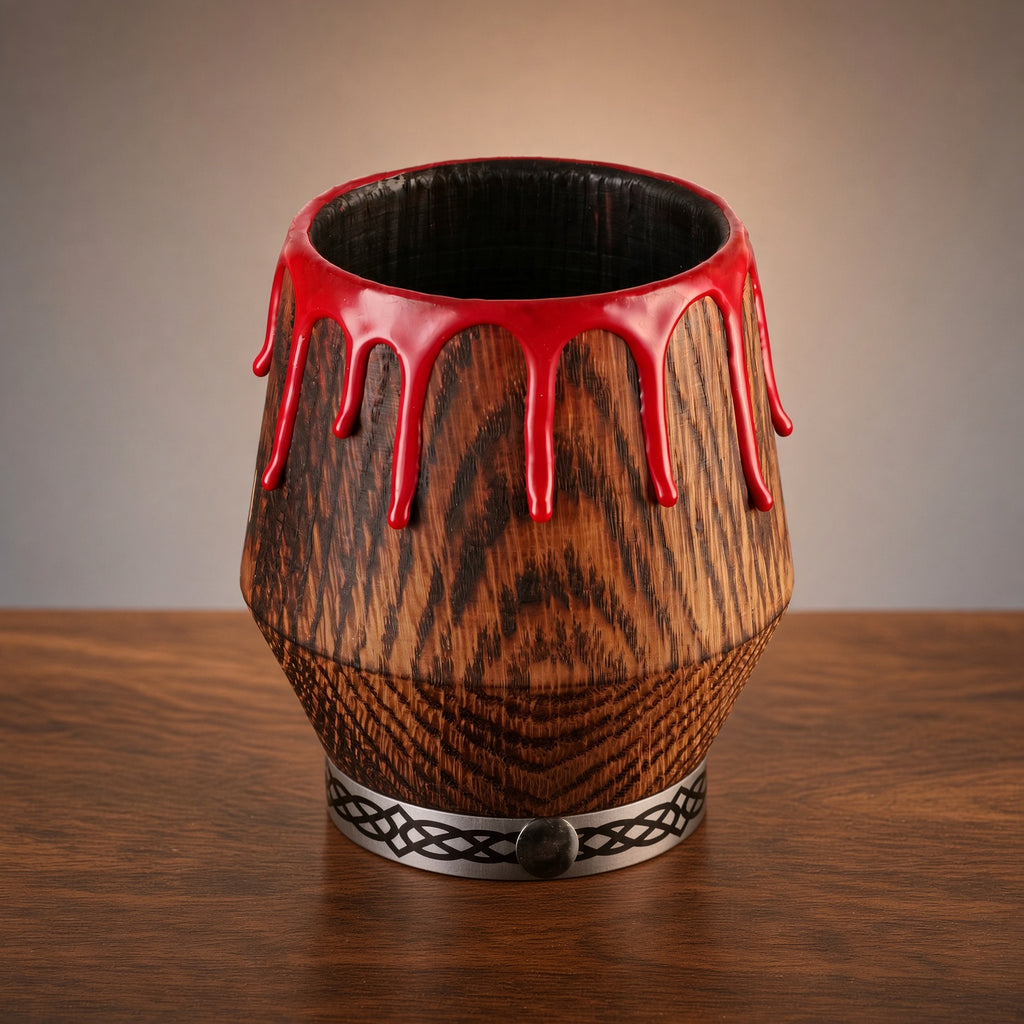 Gothic oak whiskey glass with red drips and a patterned silver base on a wooden table.