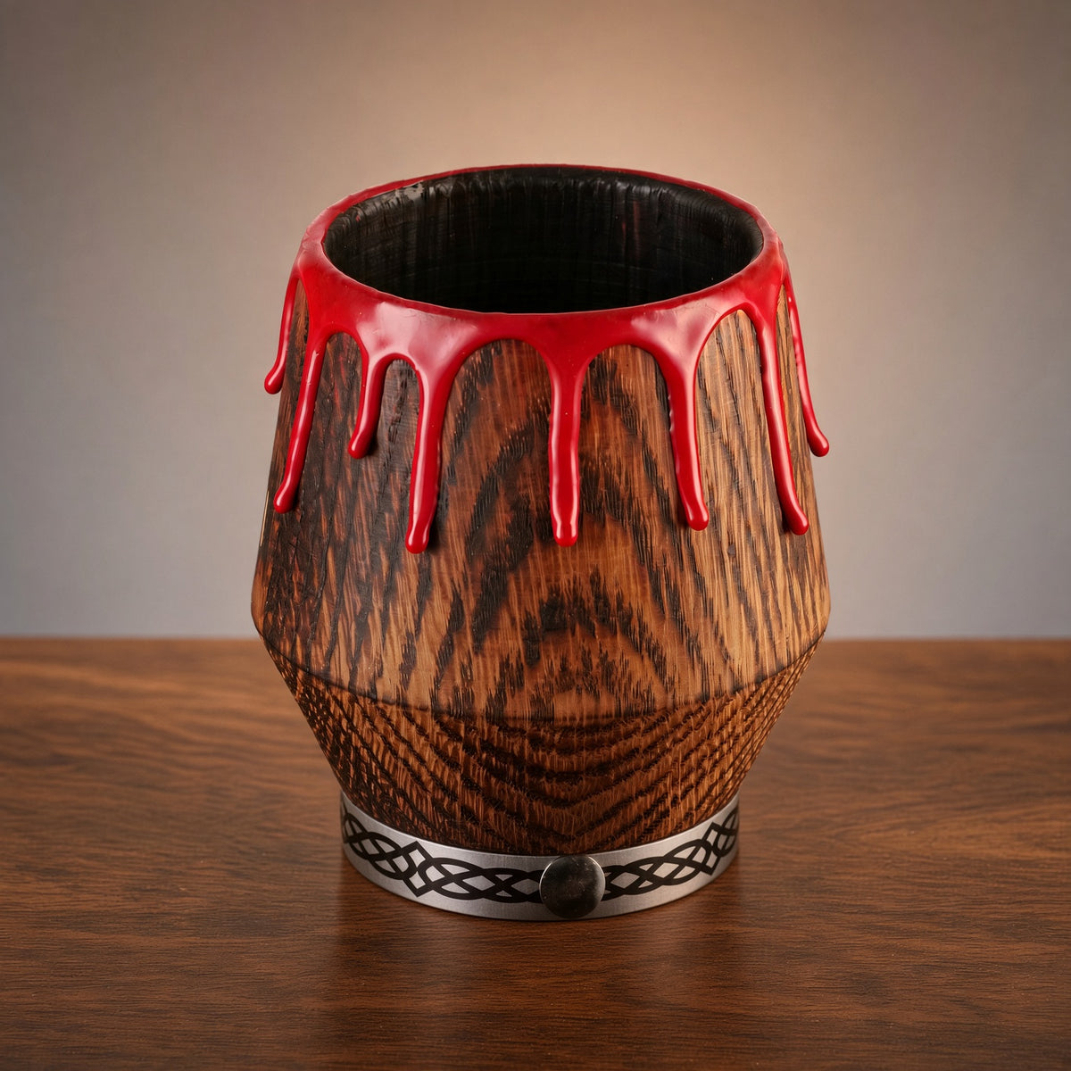 Gothic oak whiskey glass with red drips and a patterned silver base on a wooden table.