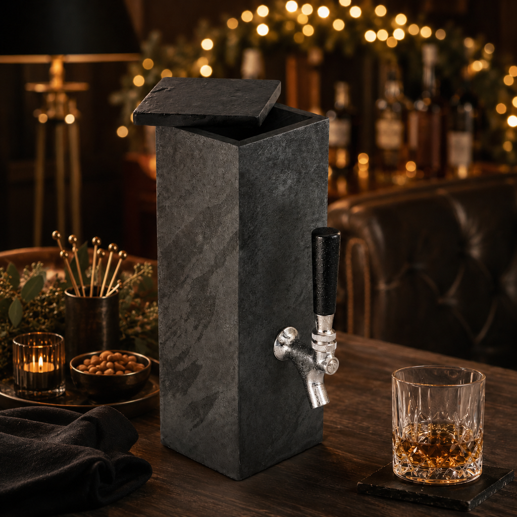 Natural black slate whiskey dispenser displayed in a warm bar setting with glass and matching coaster
