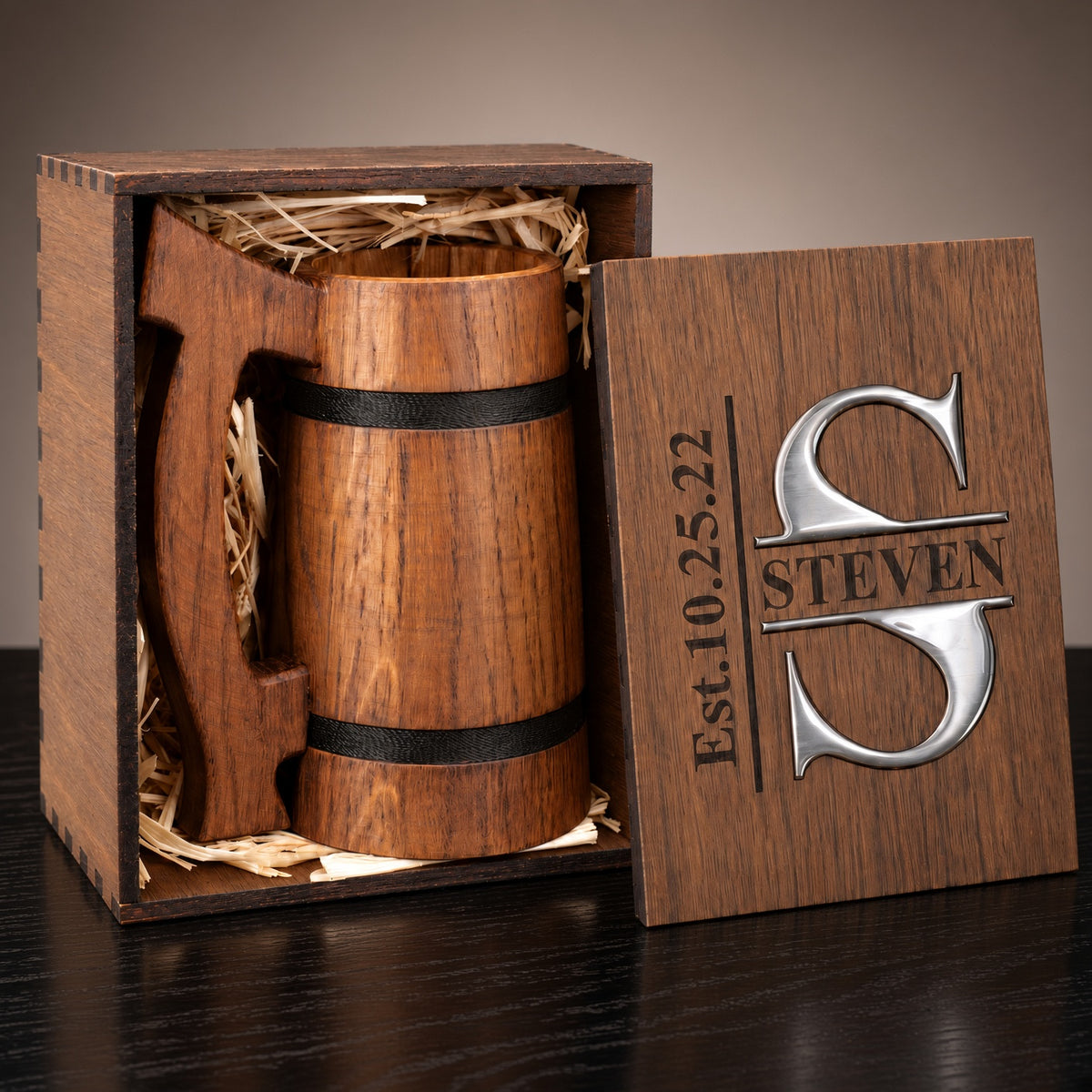 Oak beer mug packed in a wooden gift box with straw filler, beside a personalized lid with a silver-colored S monogram.