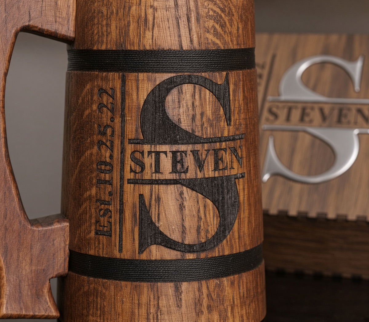 Close-up of the Steven split monogram engraved directly into an oak beer mug between two decorative black bands.