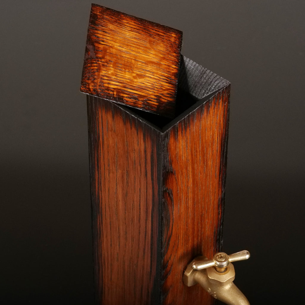 Close-up of the oak whiskey dispenser with its thin wooden lid raised, revealing the charred opening and rich exterior wood grain.