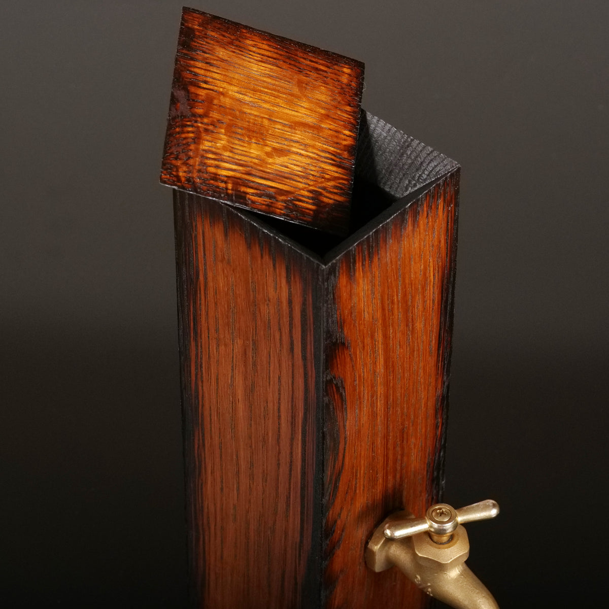 Close-up of the oak whiskey dispenser with its thin wooden lid raised, revealing the charred opening and rich exterior wood grain.