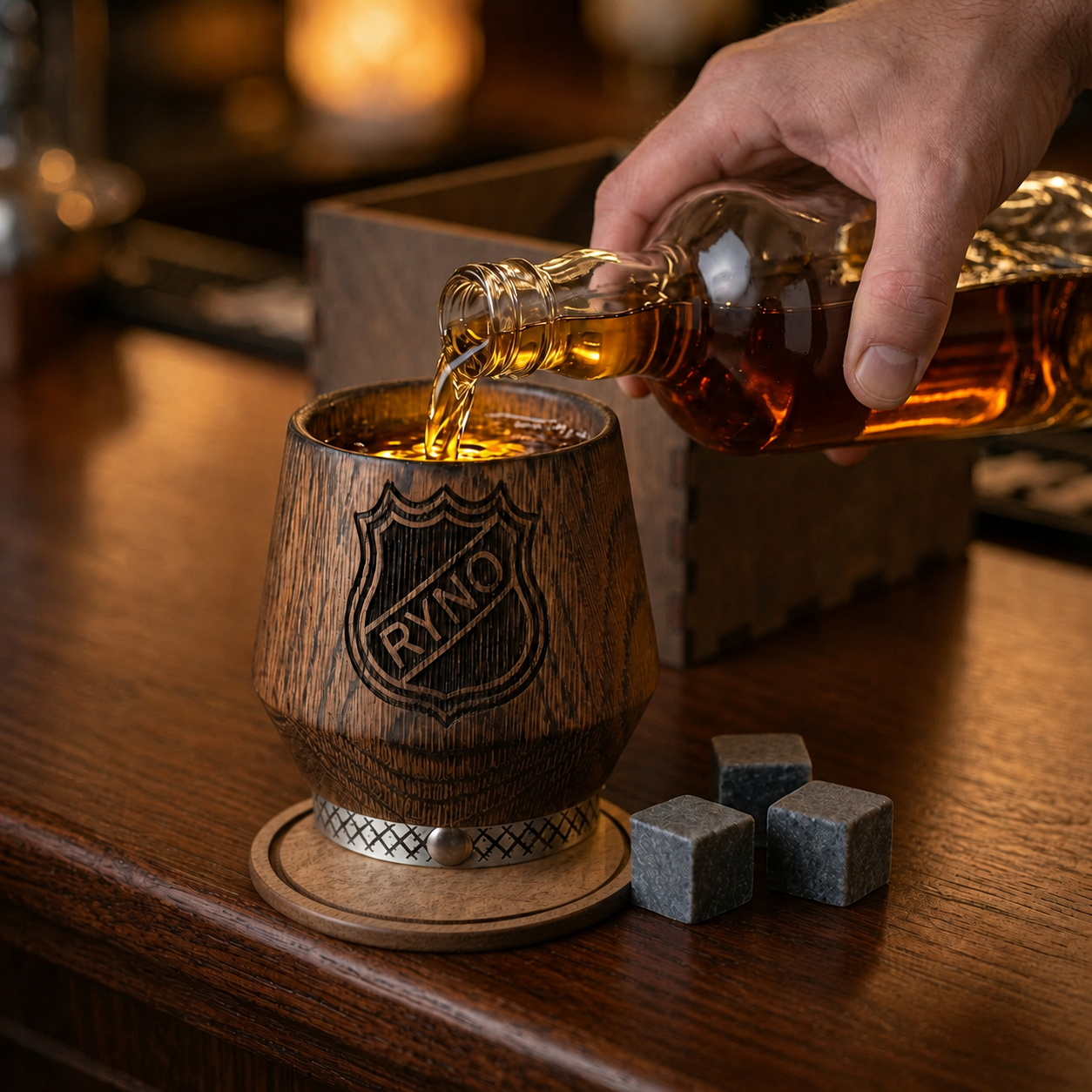 Hand holding a personalized oak whiskey tumbler above a wooden coaster in a warm home bar