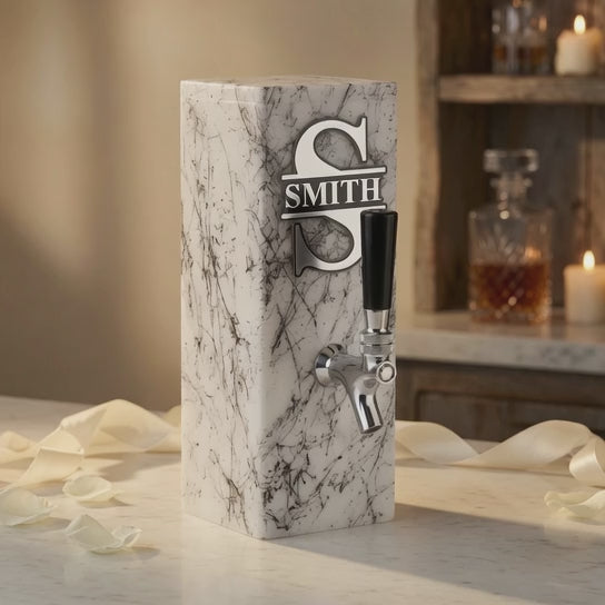 Video of a personalized white marble whiskey dispenser with engraved plaque, shown in a warm home bar setting with a whiskey glass.