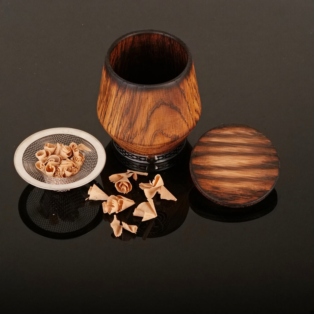 Complete whiskey smoker kit on black background with oak glass, wooden lid, smoking insert, and oak chips.