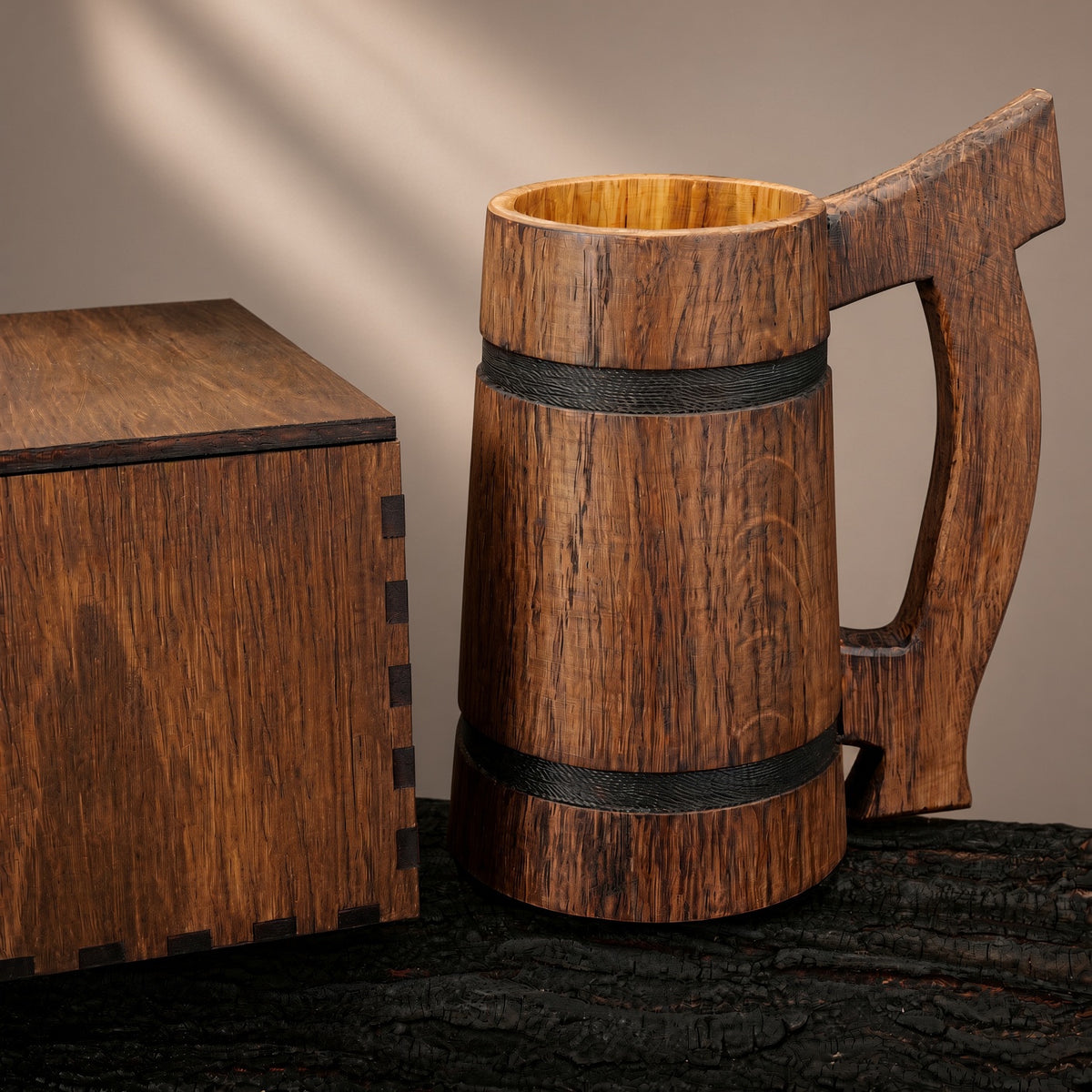 Rear view of an oak beer mug showing the natural wood grain, wooden handle, and two black bands beside its gift box.